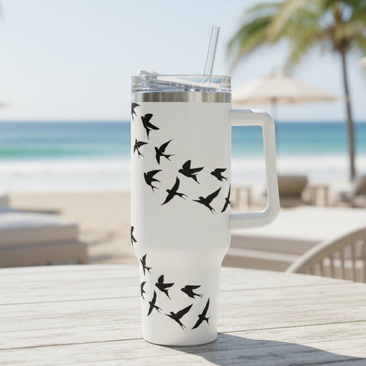 White tumbler with black bird design on a table at a beachside location.
