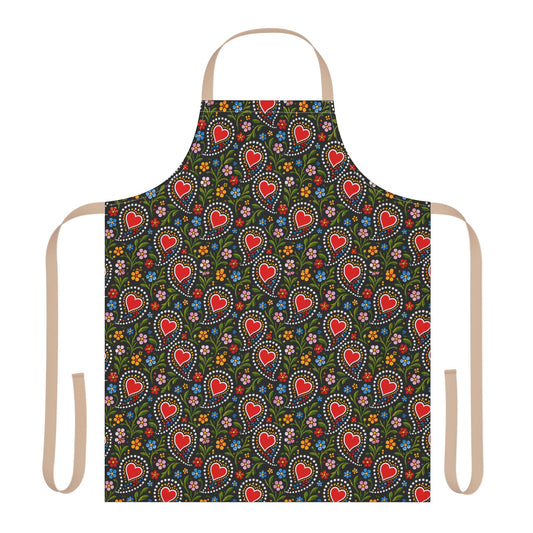 A flat-lay view of a kitchen apron with a dark green background covered in a colorful pattern of red hearts, white dotted circles, and small flowers. The apron has beige neck and waist straps on a solid white background.