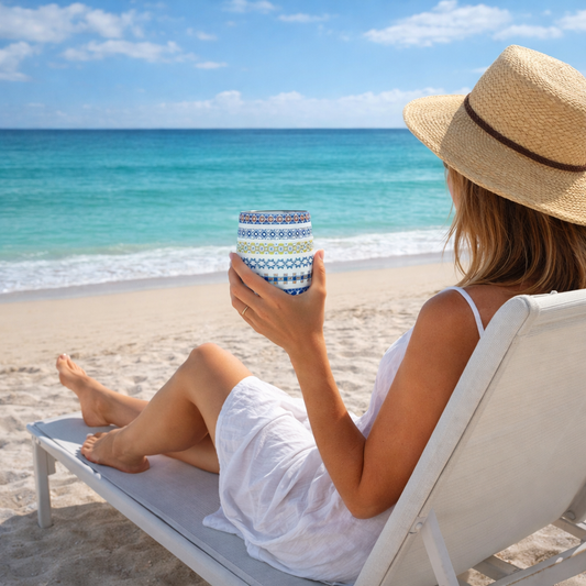 Woman sitting on a beach chair holding a colorful Faixa wine tumbler, looking at the ocean.