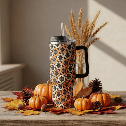 40 oz stainless steel tumbler with a black, orange, and cream geometric fall pattern, sitting on a rustic table surrounded by mini pumpkins, pinecones, and autumn leaves.