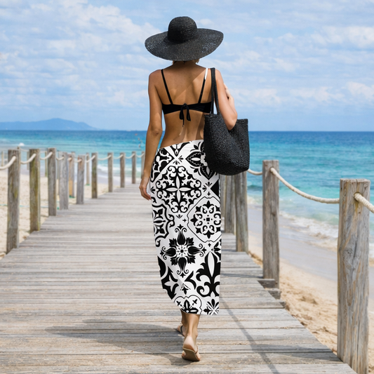 Woman walking on a wooden boardwalk towards the ocean with a black hat and patterned dress.
