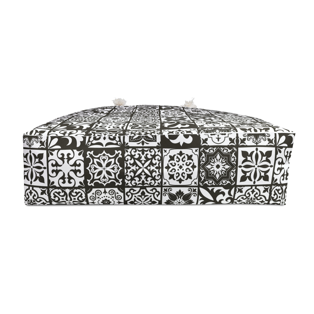 A rectangular floor cushion or ottoman upholstered in a black and white mosaic tile pattern, featuring two small white pom-poms on top, set against a plain white background.