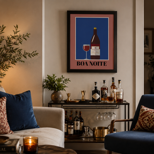 A framed wall art print featuring a wine bottle and glass on a blue background with the text 'BOA NOITE' in Portuguese, displayed in a cozy living room above a bar cart with wine bottles.