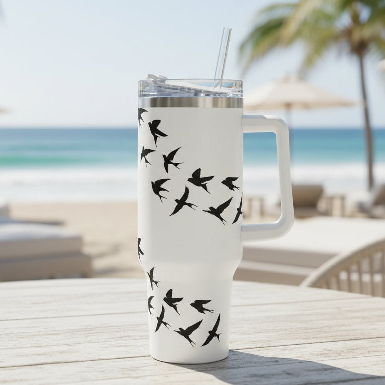 White tumbler with black bird design on a table at a beachside location.