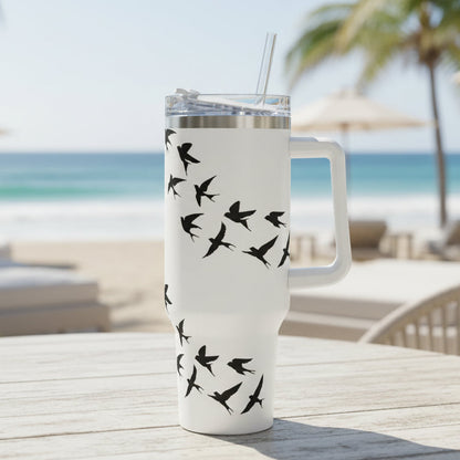 White tumbler with black bird design on a table at a beachside location.
