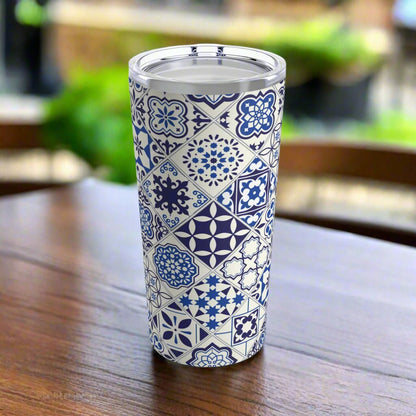 A stainless steel tumbler with a clear push-on lid featuring a geometric Portuguese tile pattern, placed on a wooden surface with blurred background.