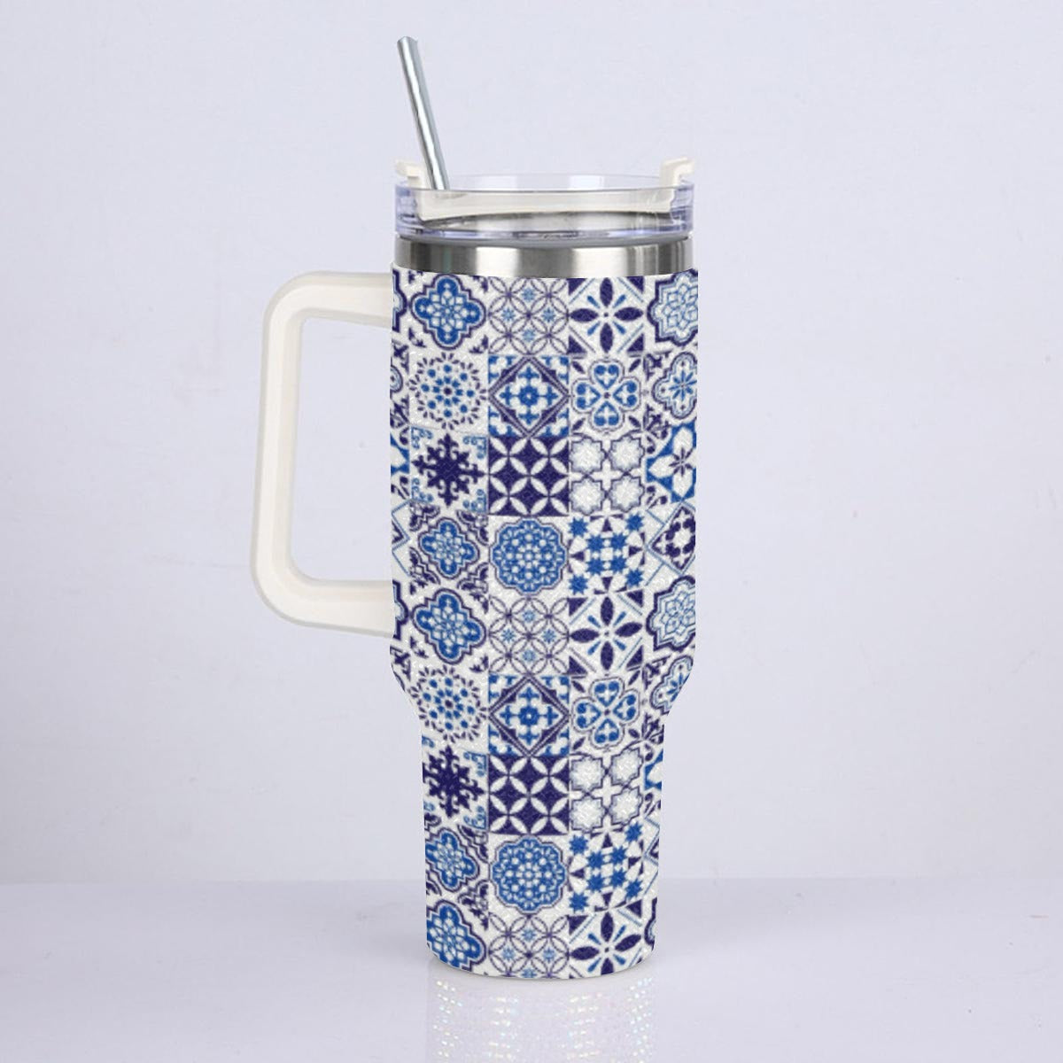 A tall handled travel tumbler with a blue and white geometric tile pattern, featuring a white handle, clear lid, and stainless steel straw.
