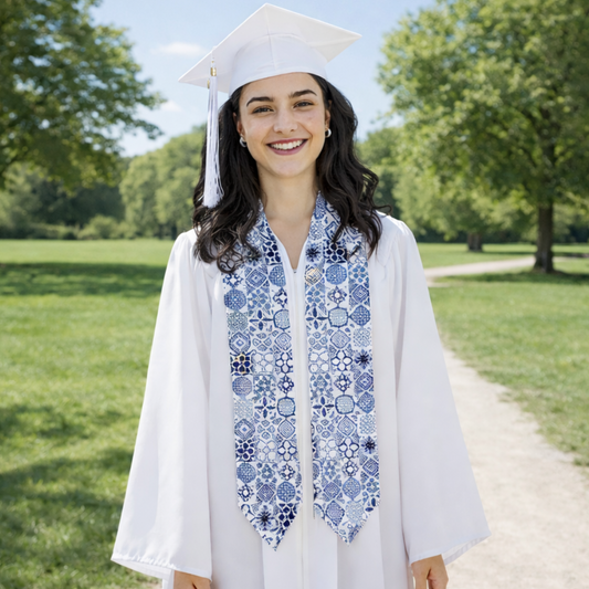 Graduate in cap and gown with decorative stole standing outdoors on a sunny day.