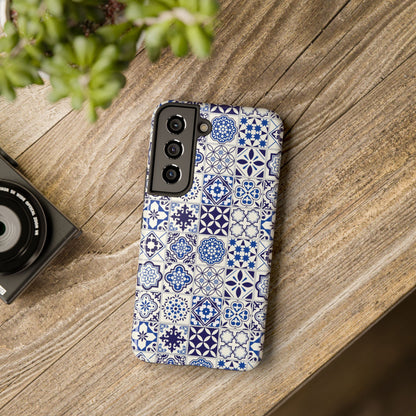 A phone case with a blue and white geometric Portuguese tile pattern, displayed on a wooden surface next to a camera.