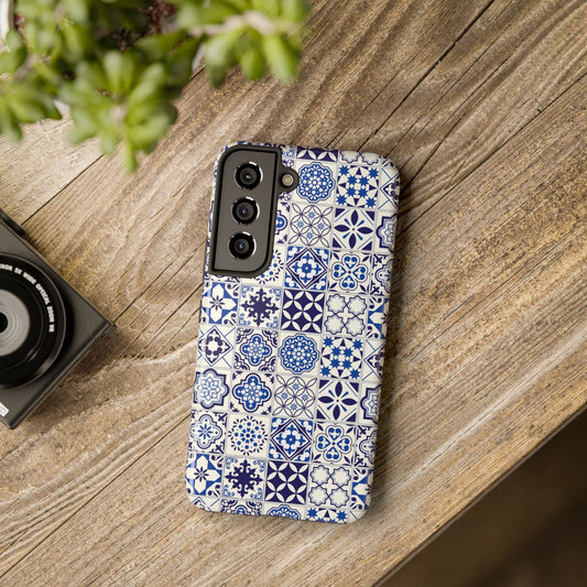 A phone case with a blue and white geometric Portuguese tile pattern, displayed on a wooden surface next to a camera.