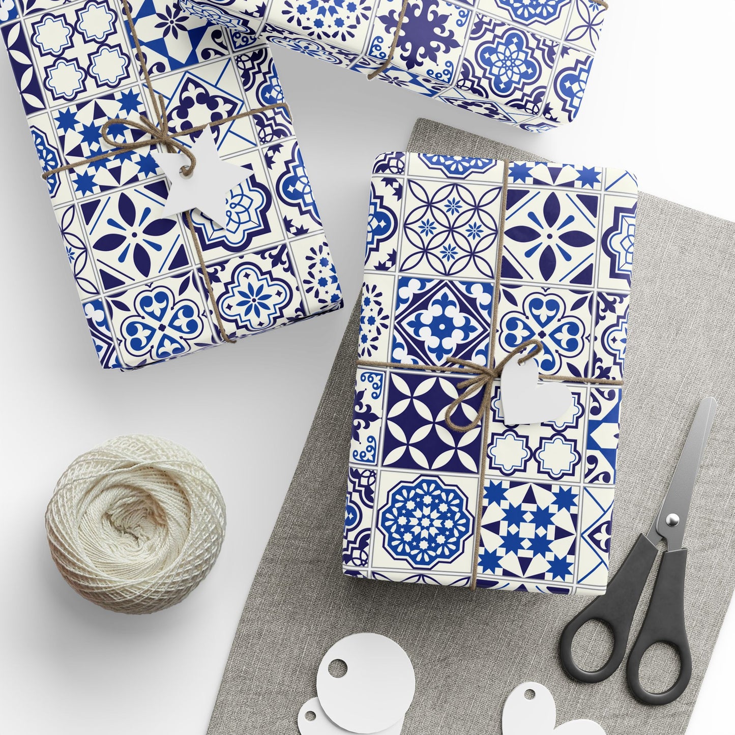 Gift boxes with blue and white azulejo patterned wrapping paper, scissors, and yarn on a gray surface.