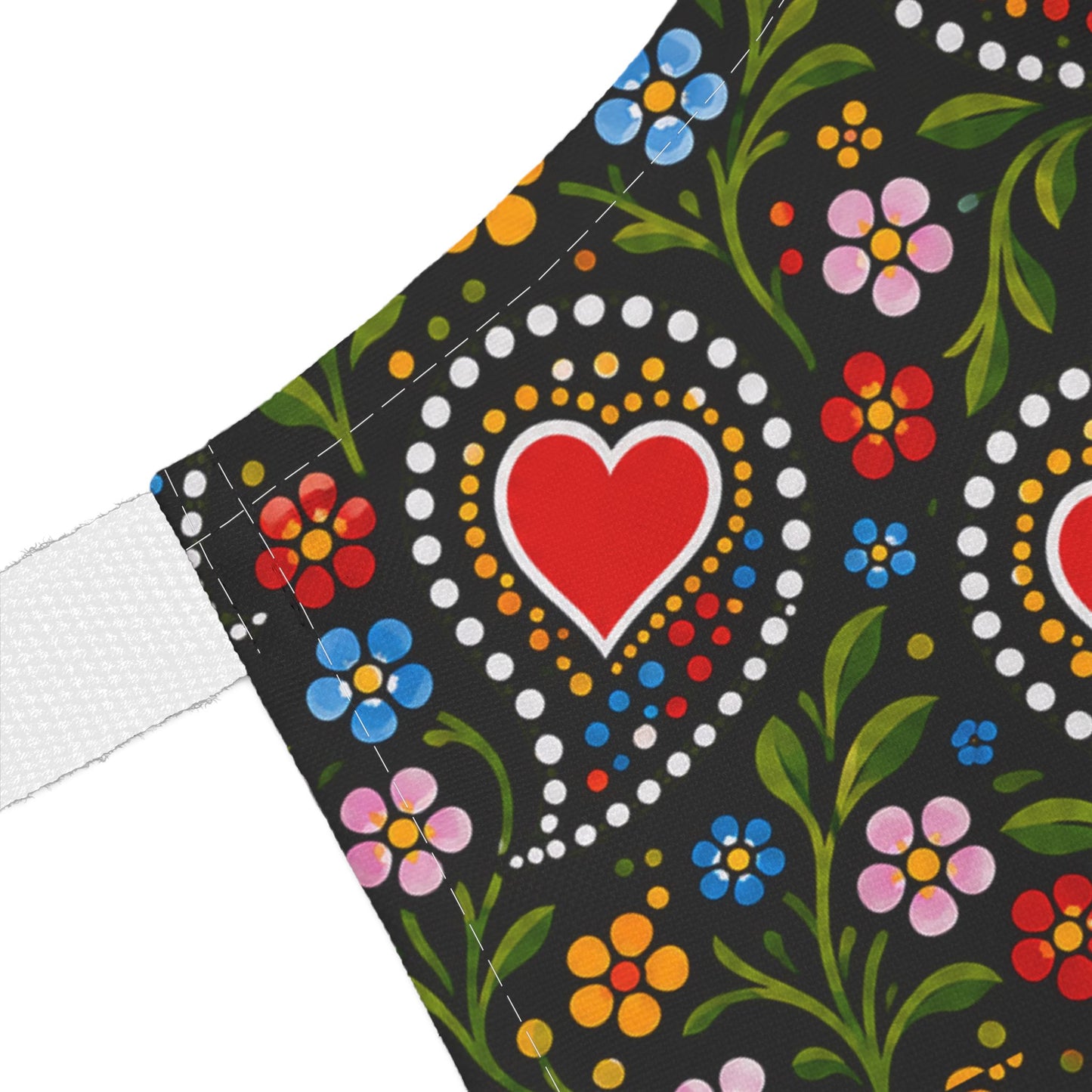 Close-up of a black fabric product with a colorful folk-art floral pattern, including a red heart motif, green leaves, and white mesh trim along the side.