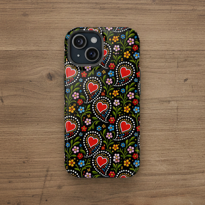 A phone case featuring a traditional Swedish folk art pattern with red hearts, white dots, and colorful flowers on a black background, shown on a plain white studio background.