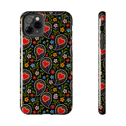 A phone case shown from the back and side on a plain white background. The case has a black base with a colorful folk-art style pattern featuring red hearts, green leaves, and small multicolored flowers.