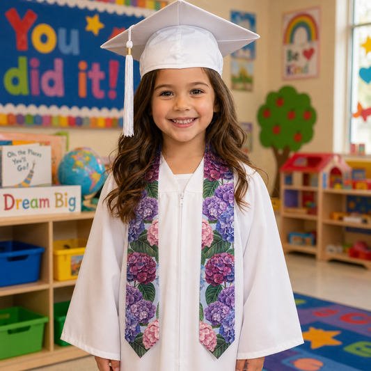 Young girl in a graduation cap and gown with a floral stole in a classroom setting.