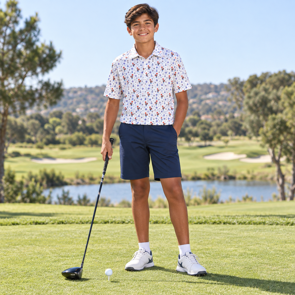 A young man stands on a golf course wearing a white short-sleeve polo shirt with a colorful floral pattern, navy blue golf shorts, white golf shoes, and holding a golf club.