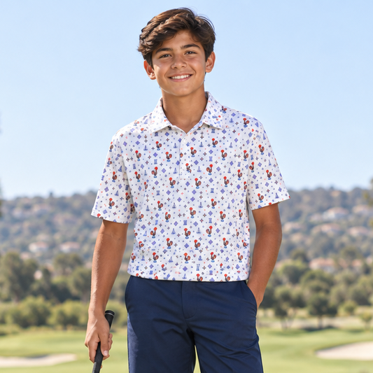 A young man stands on a golf course wearing a white short-sleeve polo shirt with a colorful floral pattern, navy blue golf shorts, white golf shoes, and holding a golf club.