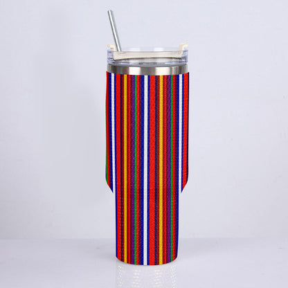 A tall insulated tumbler with a clear lid and metal straw, wrapped in a colorful vertically striped fabric sleeve featuring red, orange, yellow, green, blue, and white stripes, set against a plain light gray background.
