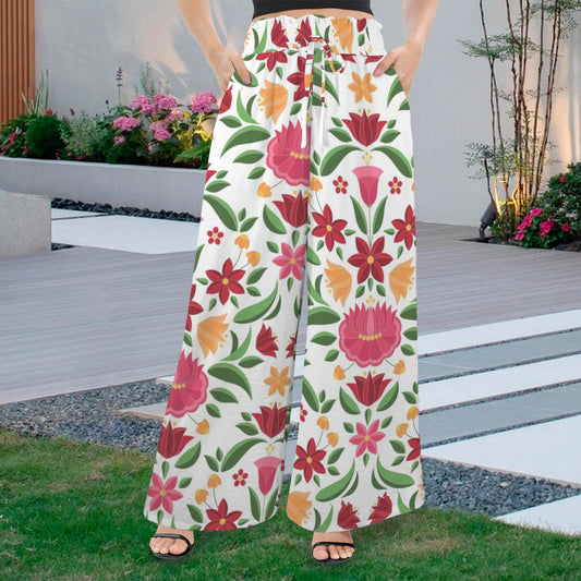 Palazzo pants featuring a vibrant Hungarian-inspired floral pattern in red, orange, and pink hues with green leaves, set against an outdoor garden backdrop.