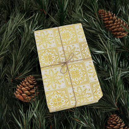 Gift wrapped in gold and white tile patterned paper with brown string on green pine needles and pine cones.