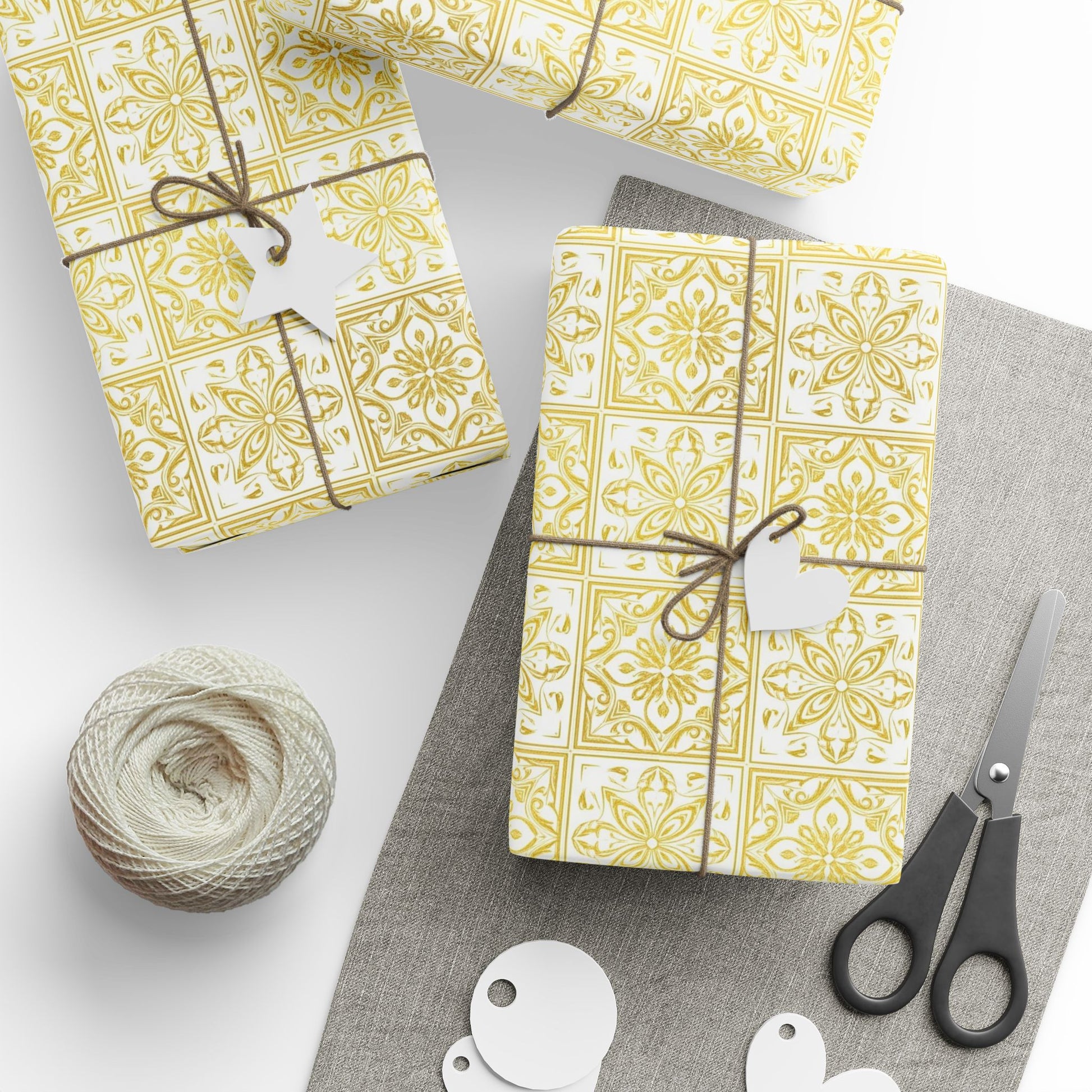 Gift boxes wrapped in yellow and white portuguese tile patterned paper with string, scissors, and a ball of twine on a gray surface.