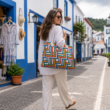 A woman walking down a cobblestone street carrying a large tote bag with a colorful geometric maze-like pattern in red, orange, yellow, green, blue, and purple.