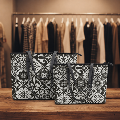 Two tote bags with a black and white geometric tile pattern are displayed on a wooden table in front of a clothing rack in a boutique setting.