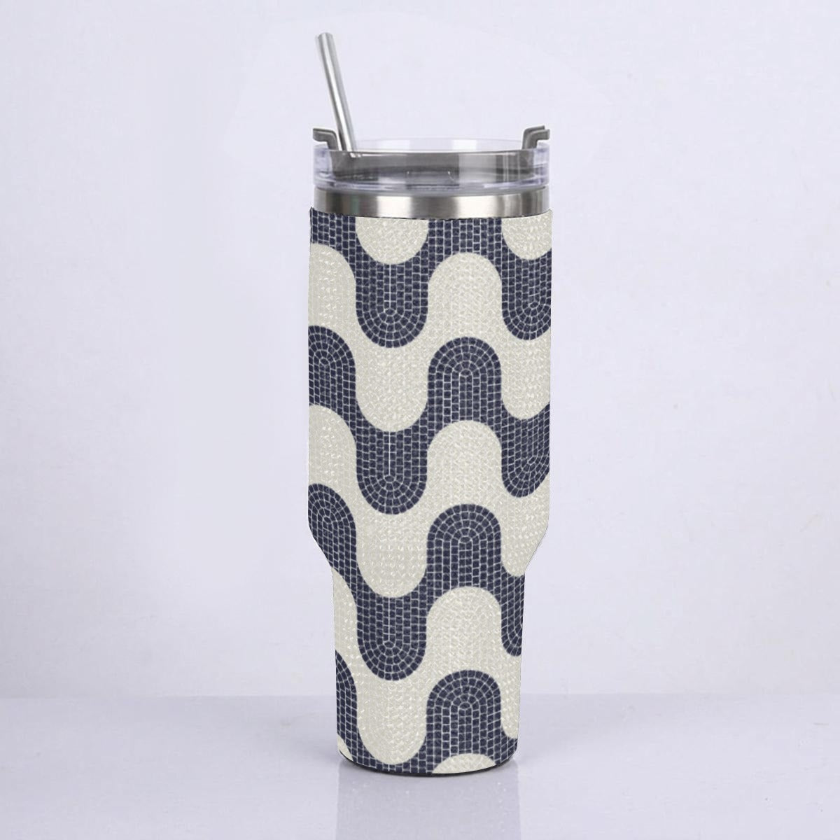 A stainless steel travel tumbler with a clear lid and straw, wrapped in a textured fabric sleeve featuring a navy blue and cream wavy geometric pattern.