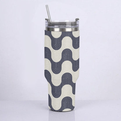 A stainless steel travel tumbler with a clear lid and straw, wrapped in a textured fabric sleeve featuring a navy blue and cream wavy geometric pattern.