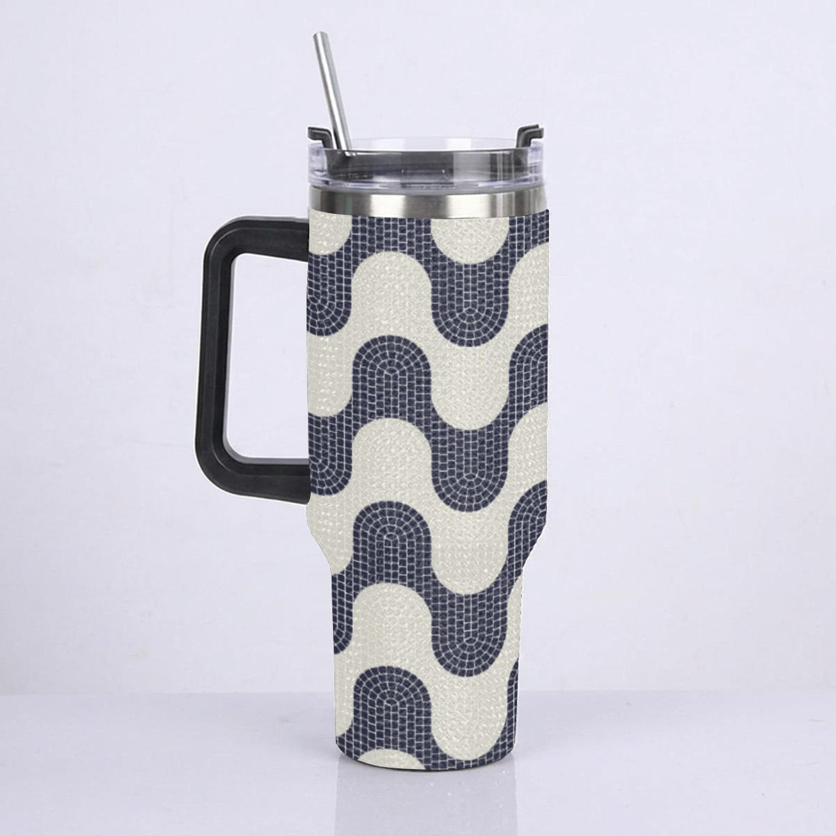 A handled insulated tumbler with a black handle and clear lid with metal straw, wrapped in a fabric sleeve featuring a navy and cream wavy geometric pattern.