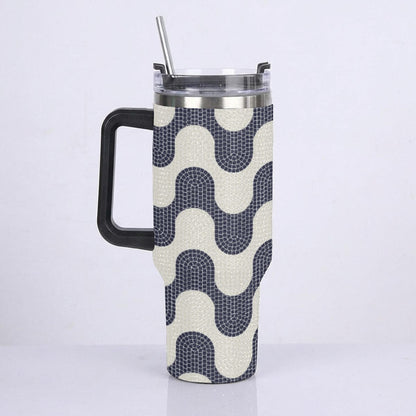 A handled insulated tumbler with a black handle and clear lid with metal straw, wrapped in a fabric sleeve featuring a navy and cream wavy geometric pattern.