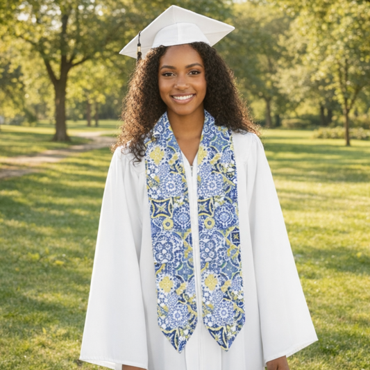 Graduate in cap and gown with a decorative stole standing outdoors on a sunny day.