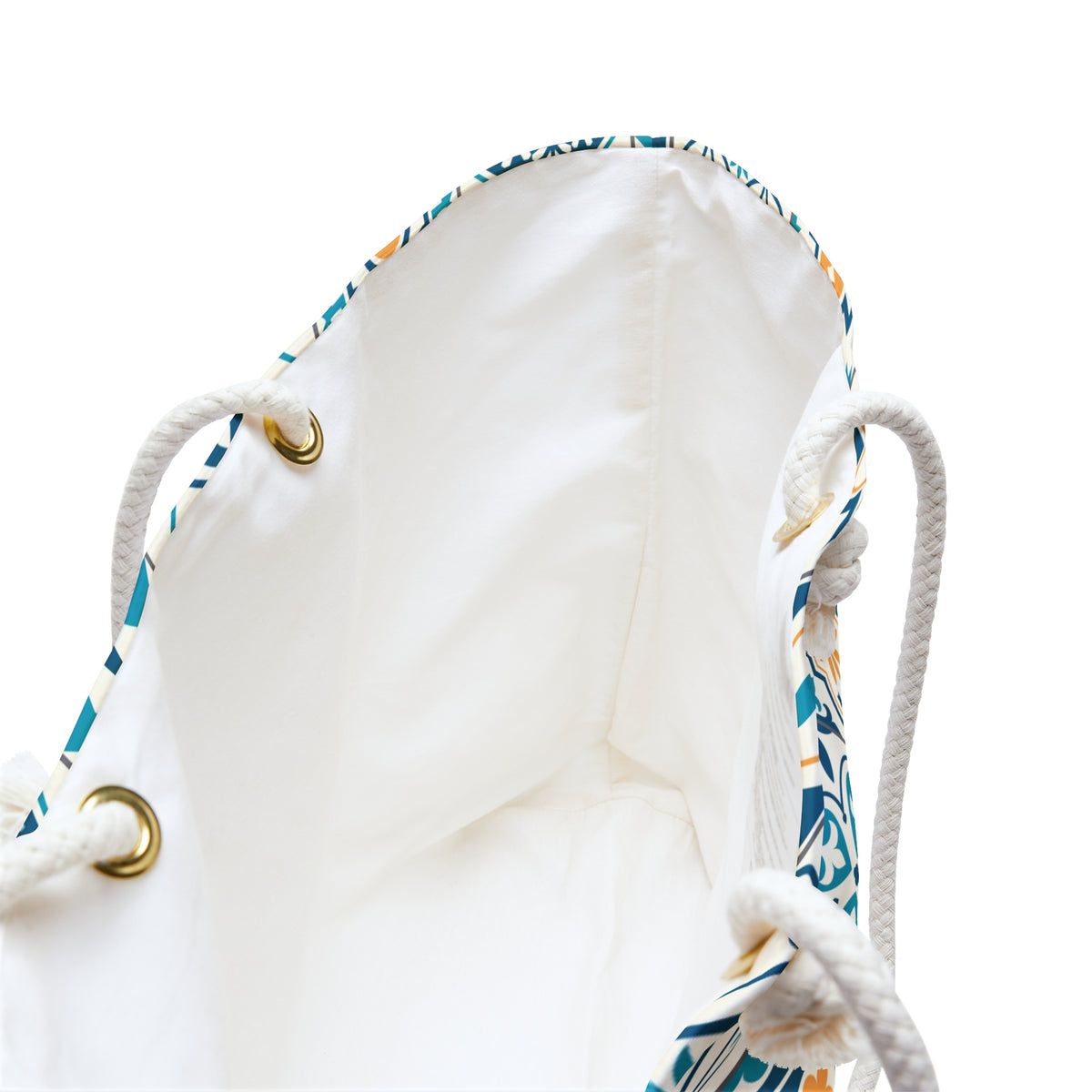 Close-up of a white drawstring bag with a blue, teal, and beige patterned trim, white rope handles, and gold-tone metal grommets on a white background.