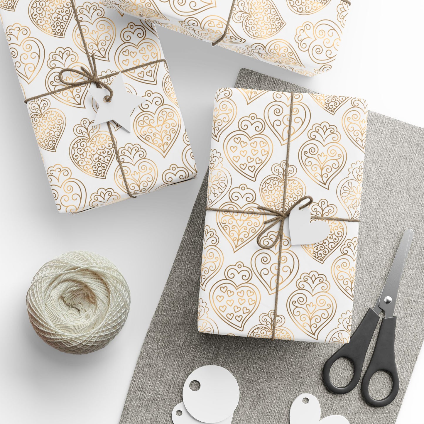 Gift boxes wrapped in gold heart of viana portugal patterned paper with string, scissors, and yarn on a white background