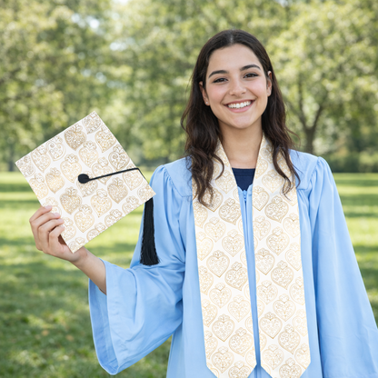 Graduate in blue gown holding a decorated diploma outdoors with greenery in the background