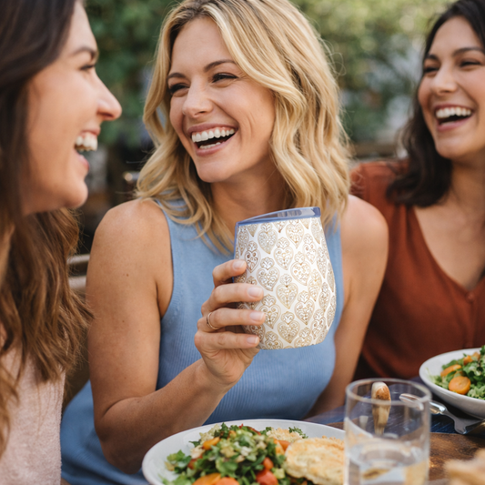 Three women enjoying a meal outdoors, smiling and laughing.