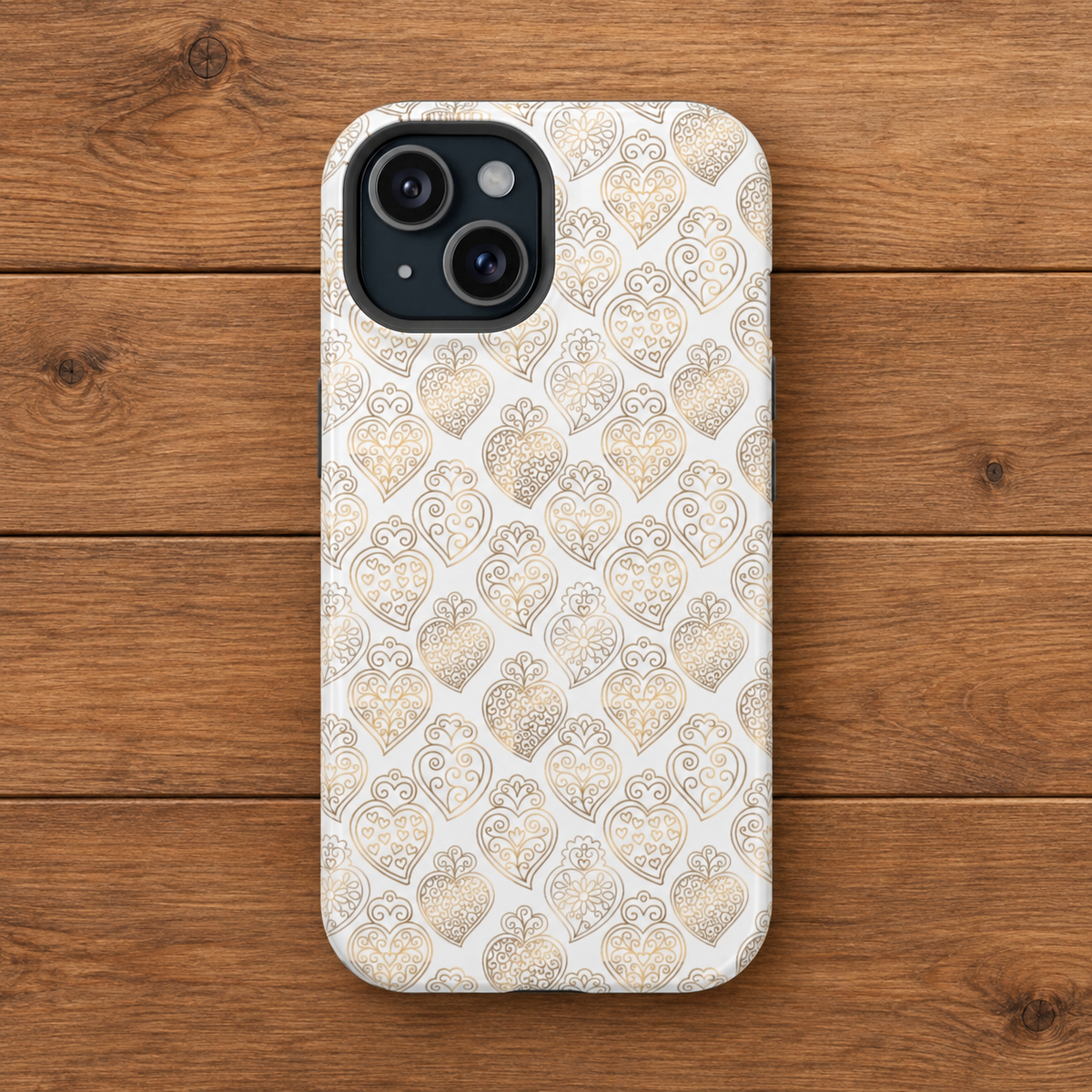 A phone case with a repeating gold heart and ornamental pattern on a white background, shown on a wooden plank surface.