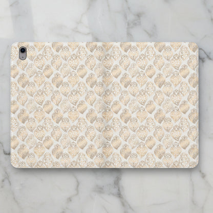 A protective iPad case featuring a repeating pattern of gold and beige hearts with ornate filigree details on a white background, shown against a solid white backdrop.