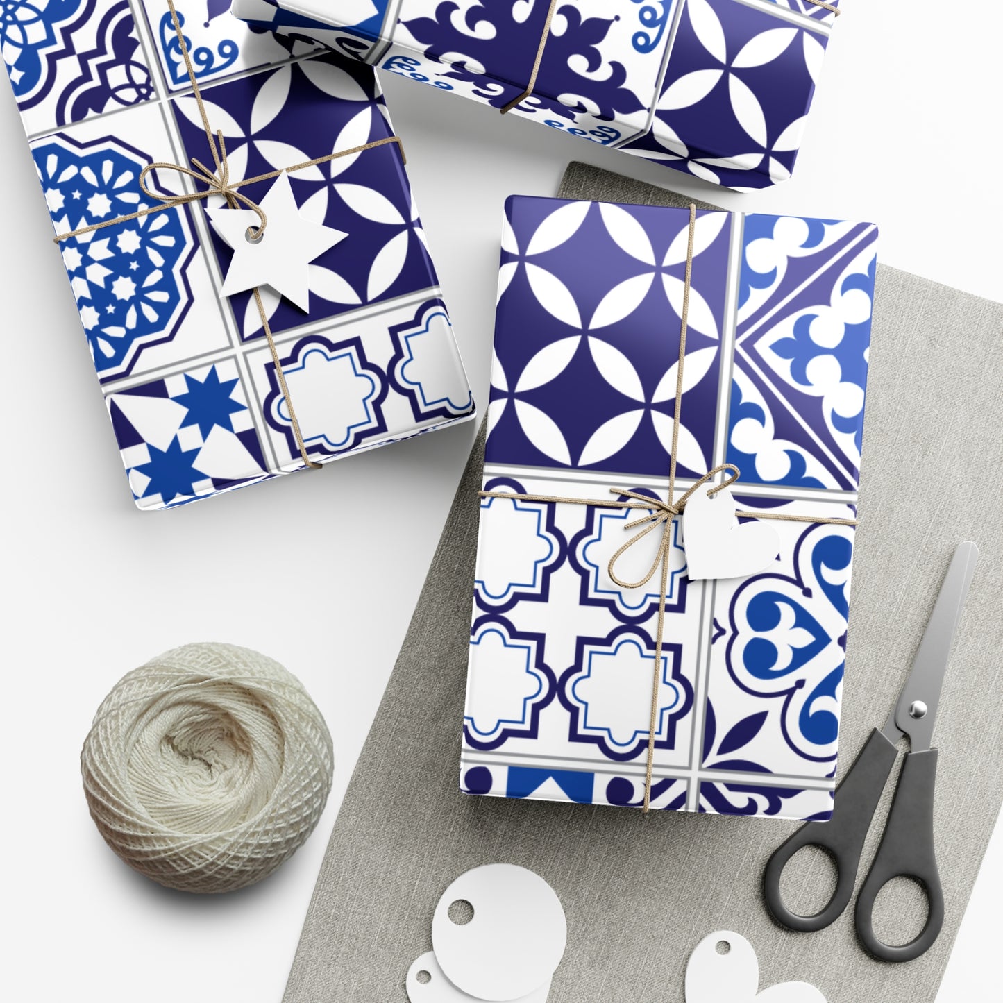 Gift boxes with blue and white patterned wrapping paper, scissors, and yarn on a white surface.