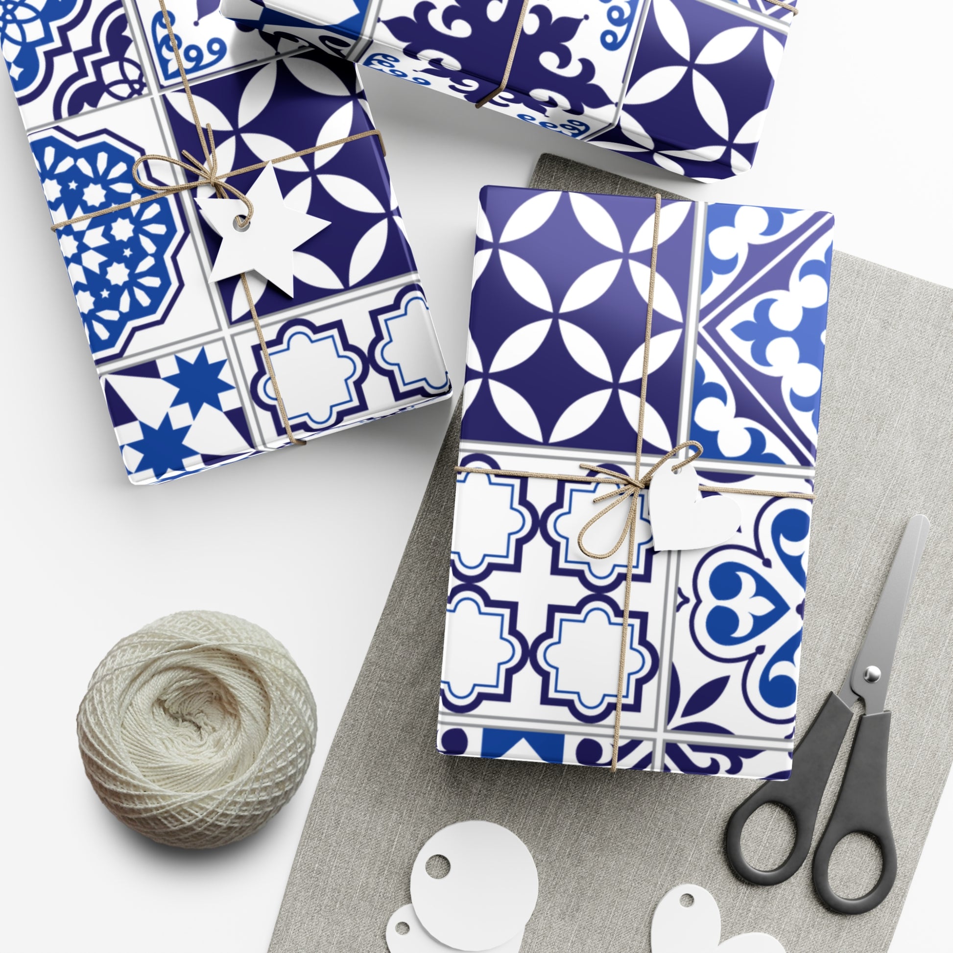Gift boxes with blue and white patterned wrapping paper, scissors, and yarn on a white surface.