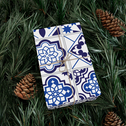 Gift wrapped in blue and white patterned paper with string, surrounded by pine branches and pinecones.
