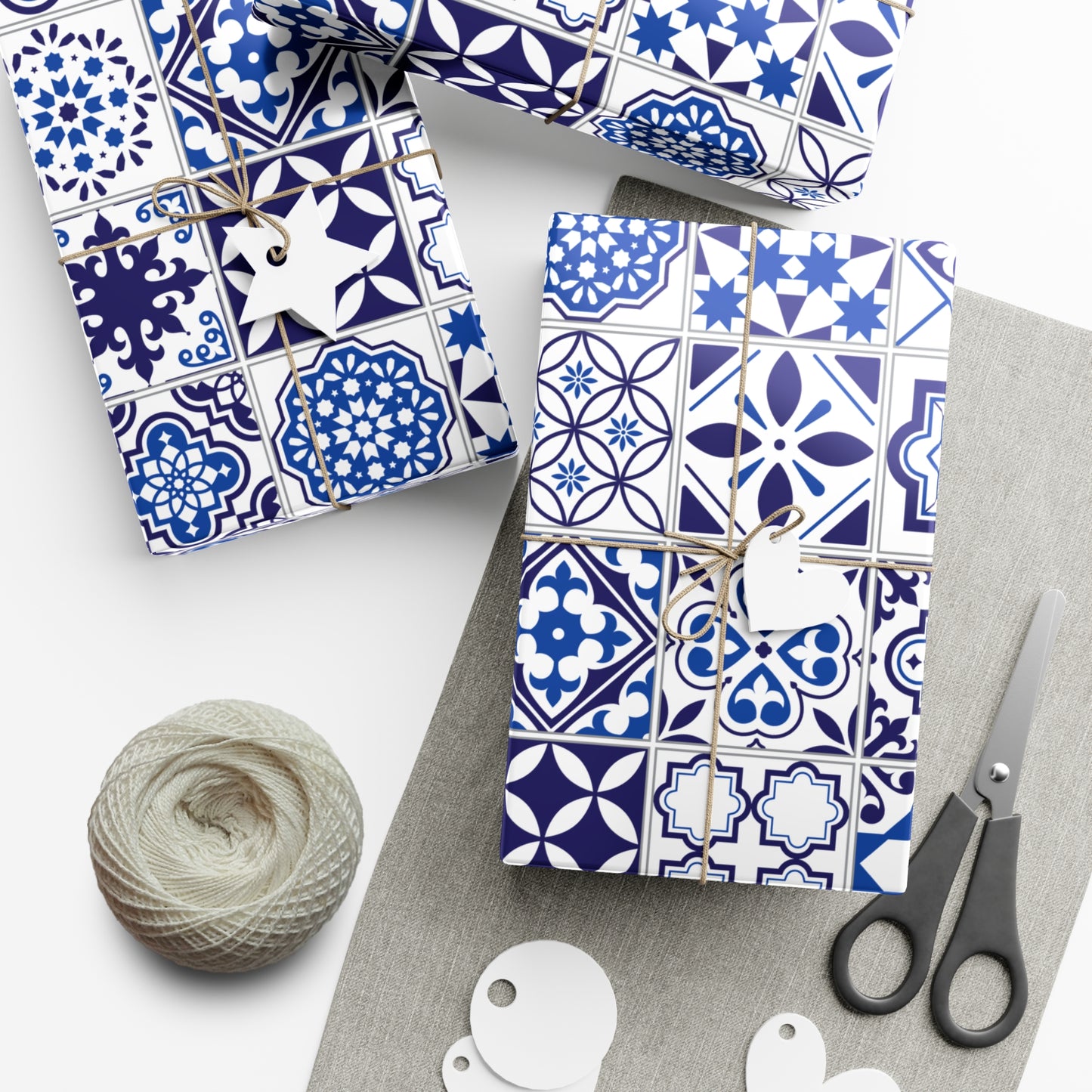 Gift boxes with blue and white patterned paper, scissors, and yarn on a white surface