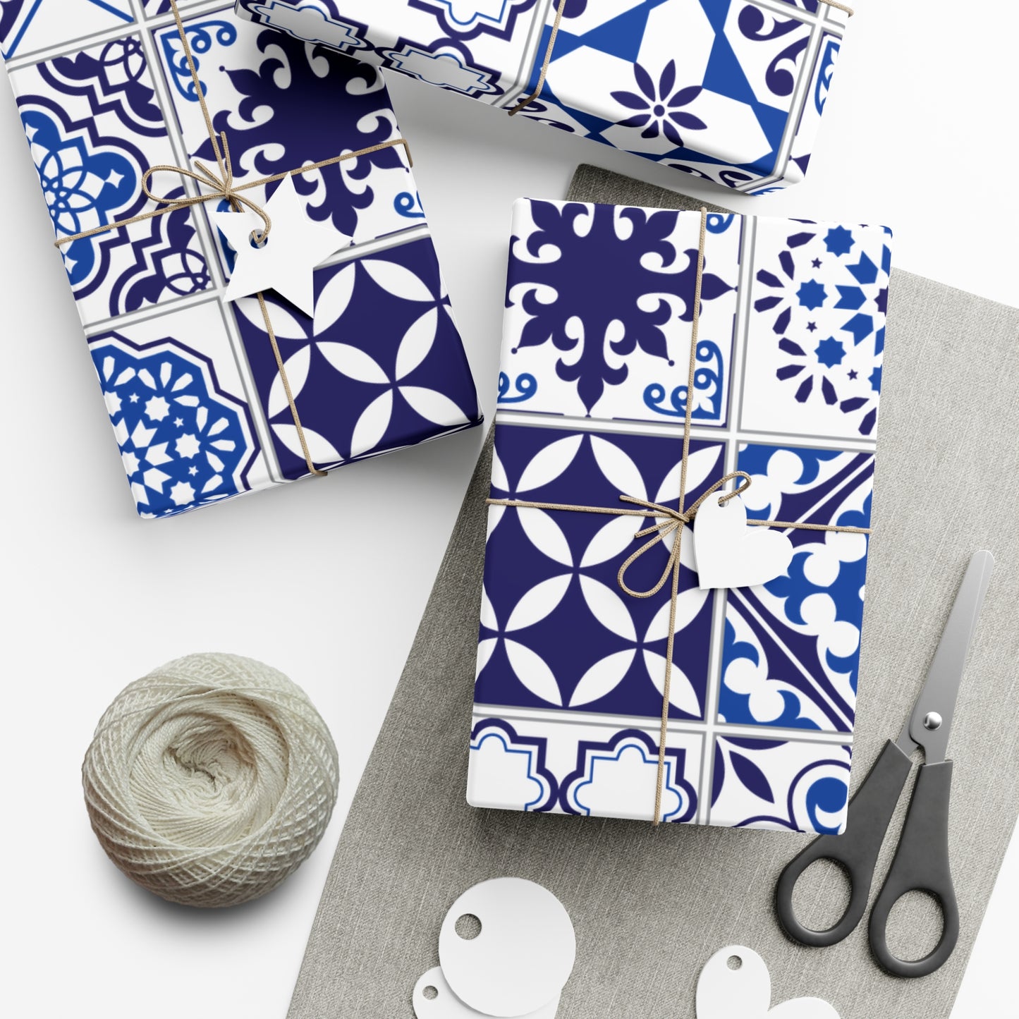 Gift boxes with blue and white patterned wrapping paper, scissors, and yarn on a white surface.
