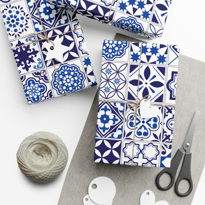 Gift boxes wrapped in blue and white tile patterned paper with scissors and yarn on a white surface