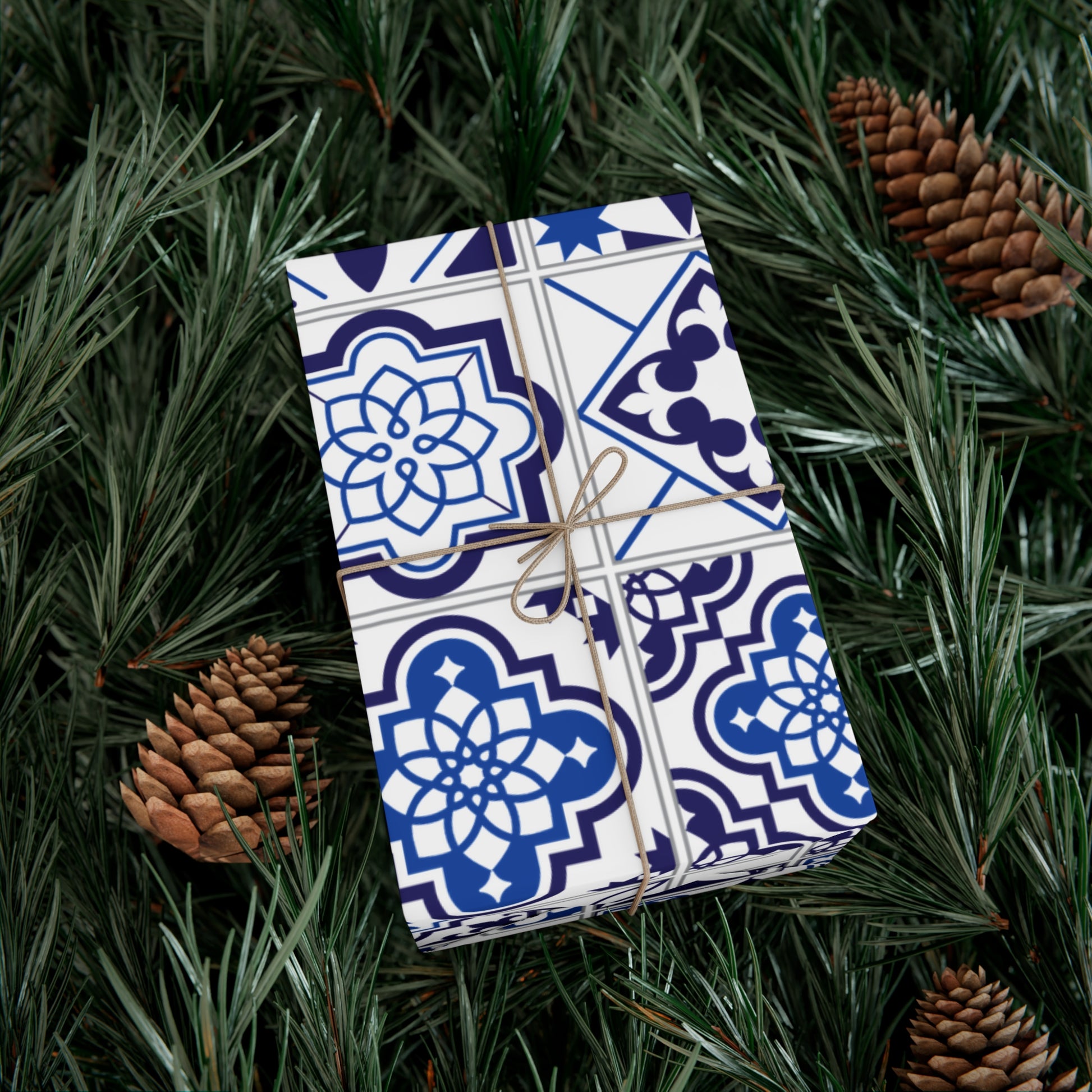 Gift wrapped in blue and white patterned paper with brown string, surrounded by pine branches and pinecones.