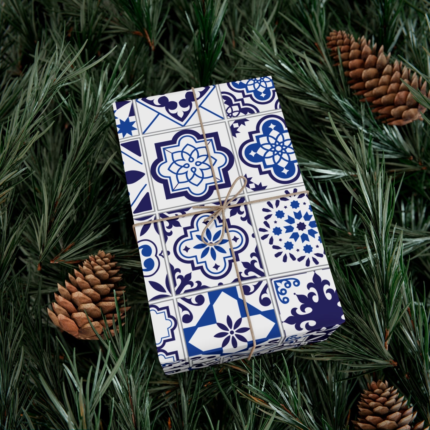 Gift wrapped in blue and white patterned paper with brown string, surrounded by pine branches and pinecones.