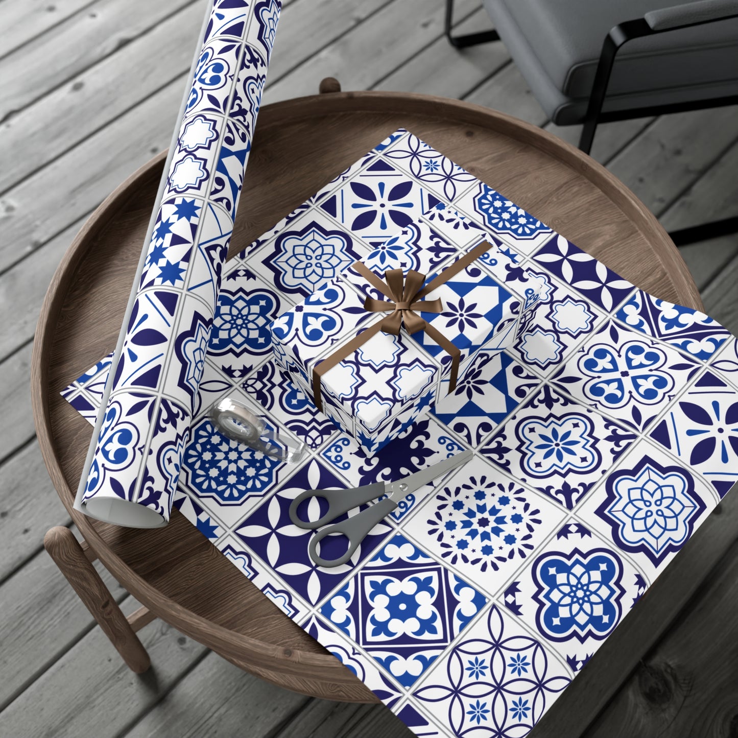 Table with blue and white patterned wrapping paper, scissors, and a roll of paper on a wooden surface.