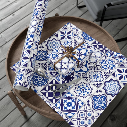 Table with blue and white patterned wrapping paper, scissors, and a roll of paper on a wooden surface.