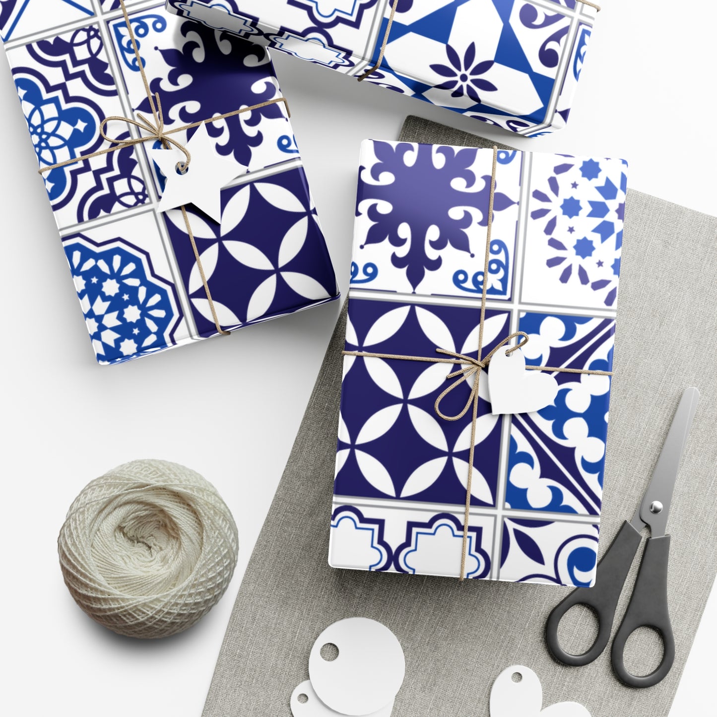 Gift boxes wrapped in blue and white patterned paper with scissors and yarn on a white surface.