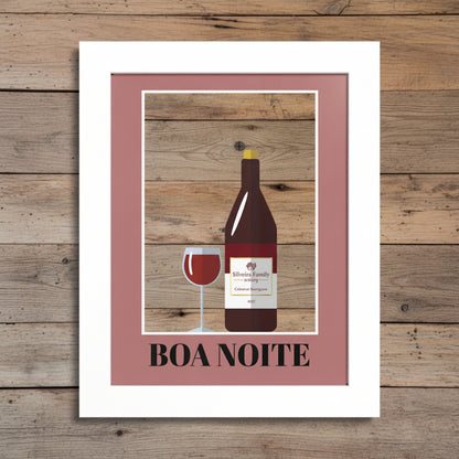 A framed art print featuring a minimalist illustration of a wine bottle and a glass of red wine against a blue background, surrounded by a dusty rose inner border and a white frame. The text 'BOA NOITE' is printed at the bottom.